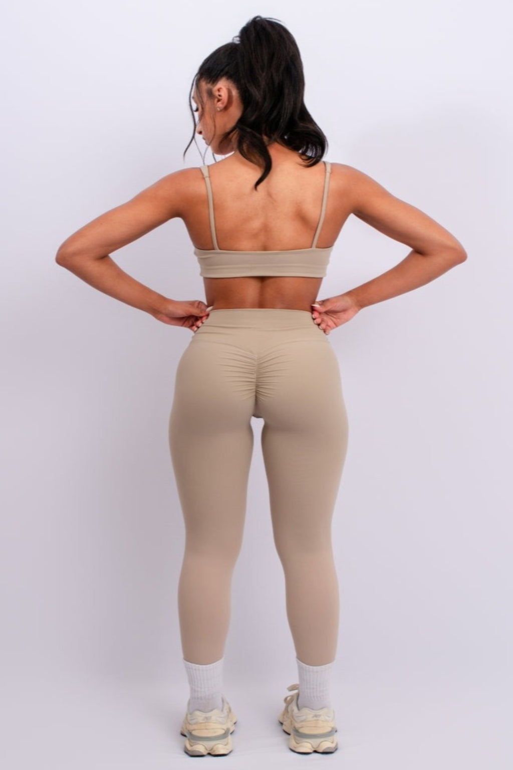 Person wearing a beige sports bra and leggings on a white background