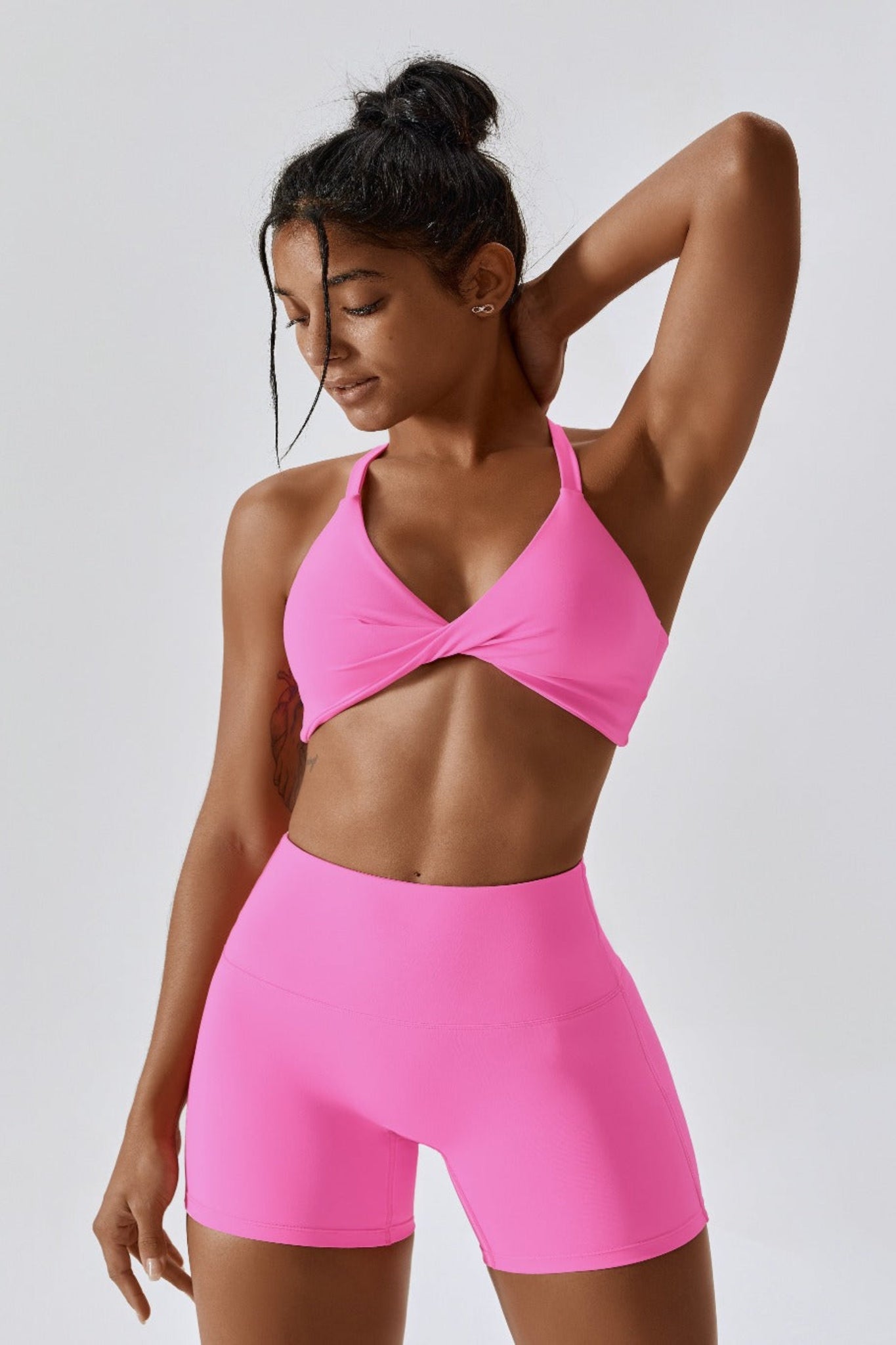 Woman wearing a bright pink sports bra and shorts set on a light gray background
