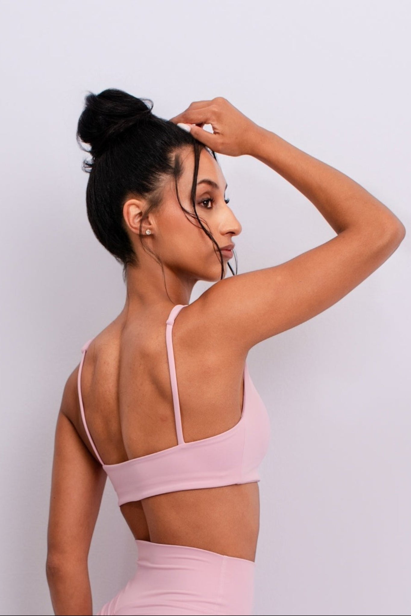 Woman wearing a pink sports bra and leggings against a light gray background