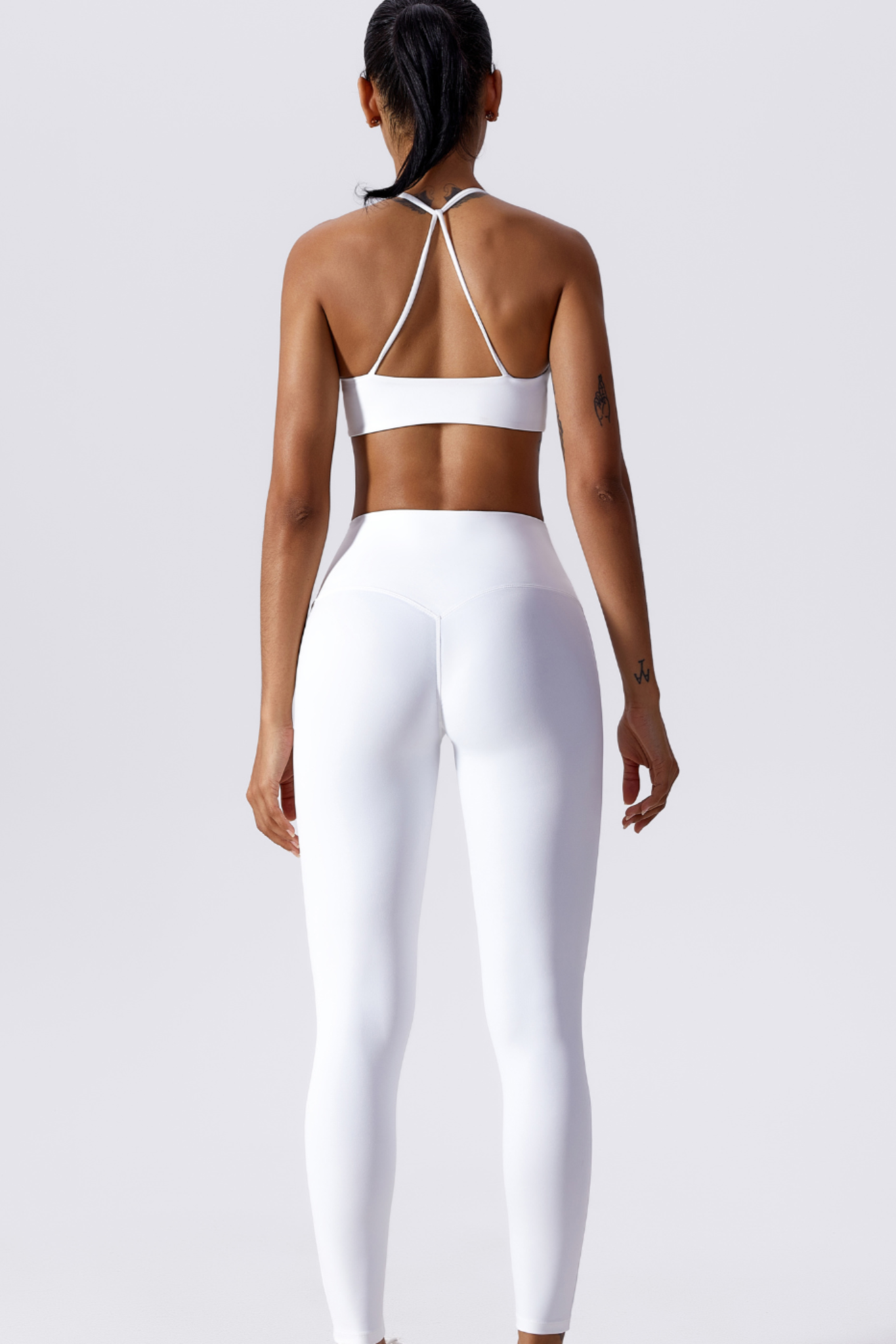 Person wearing a white sports bra and leggings set on a light gray background