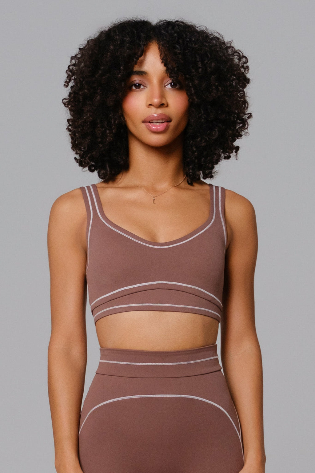 Woman wearing a Mocha brown sports bra and leggings set against a gray background