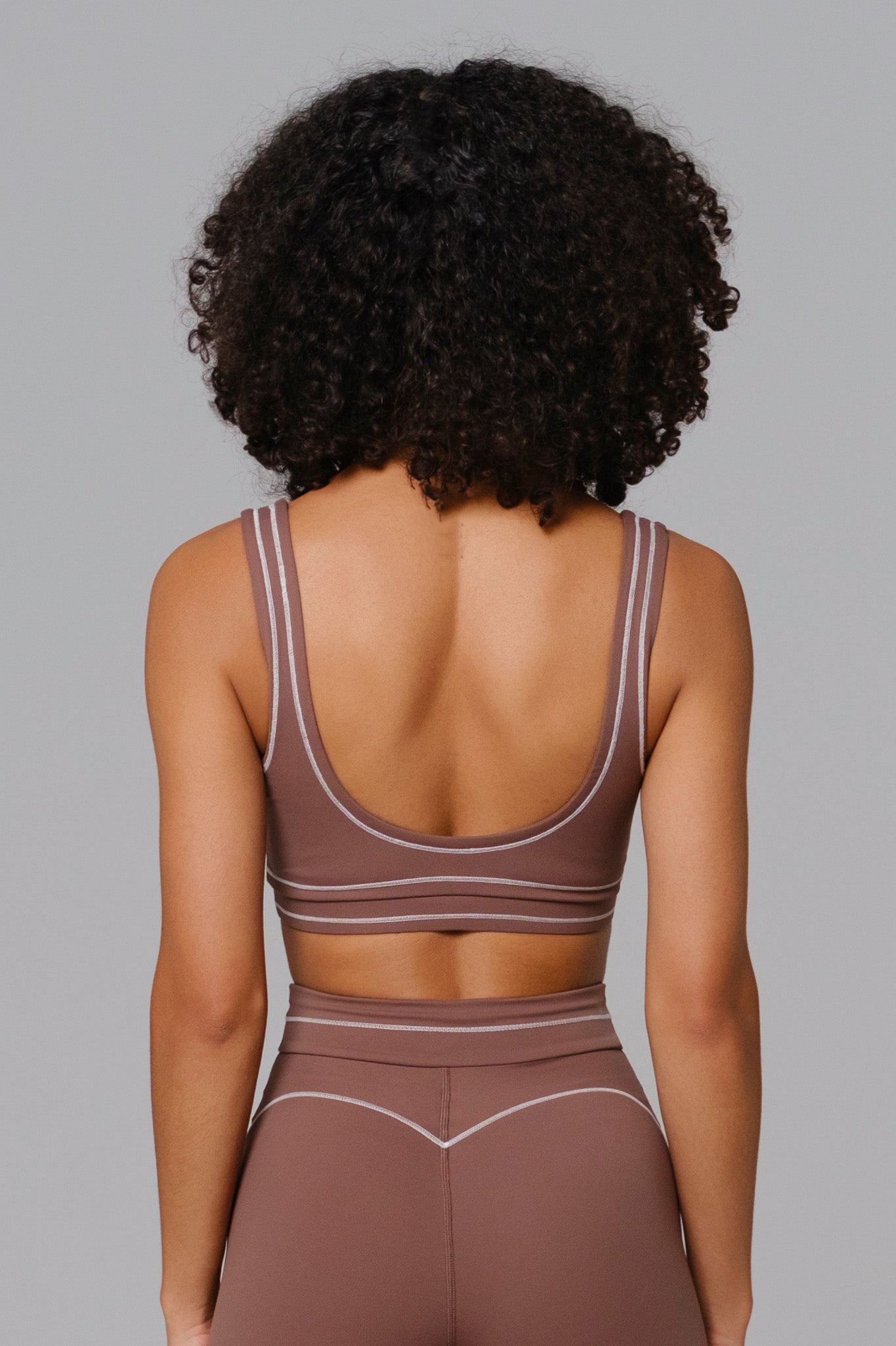 Woman wearing a Mocha brown sports bra and leggings set against a gray background