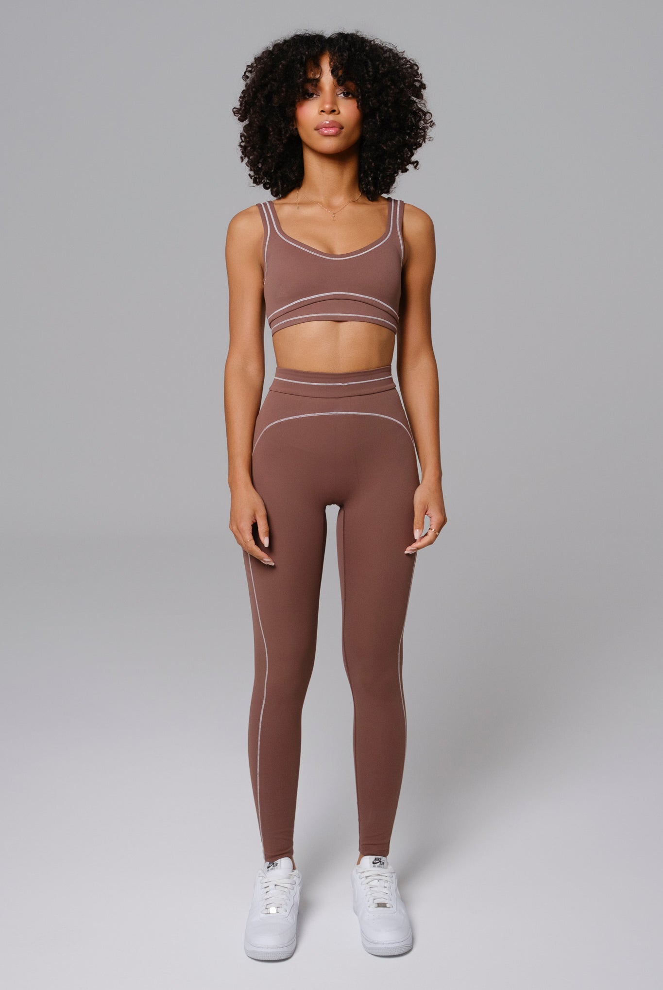 Woman wearing a Mocha brown sports bra and leggings set against a gray background
