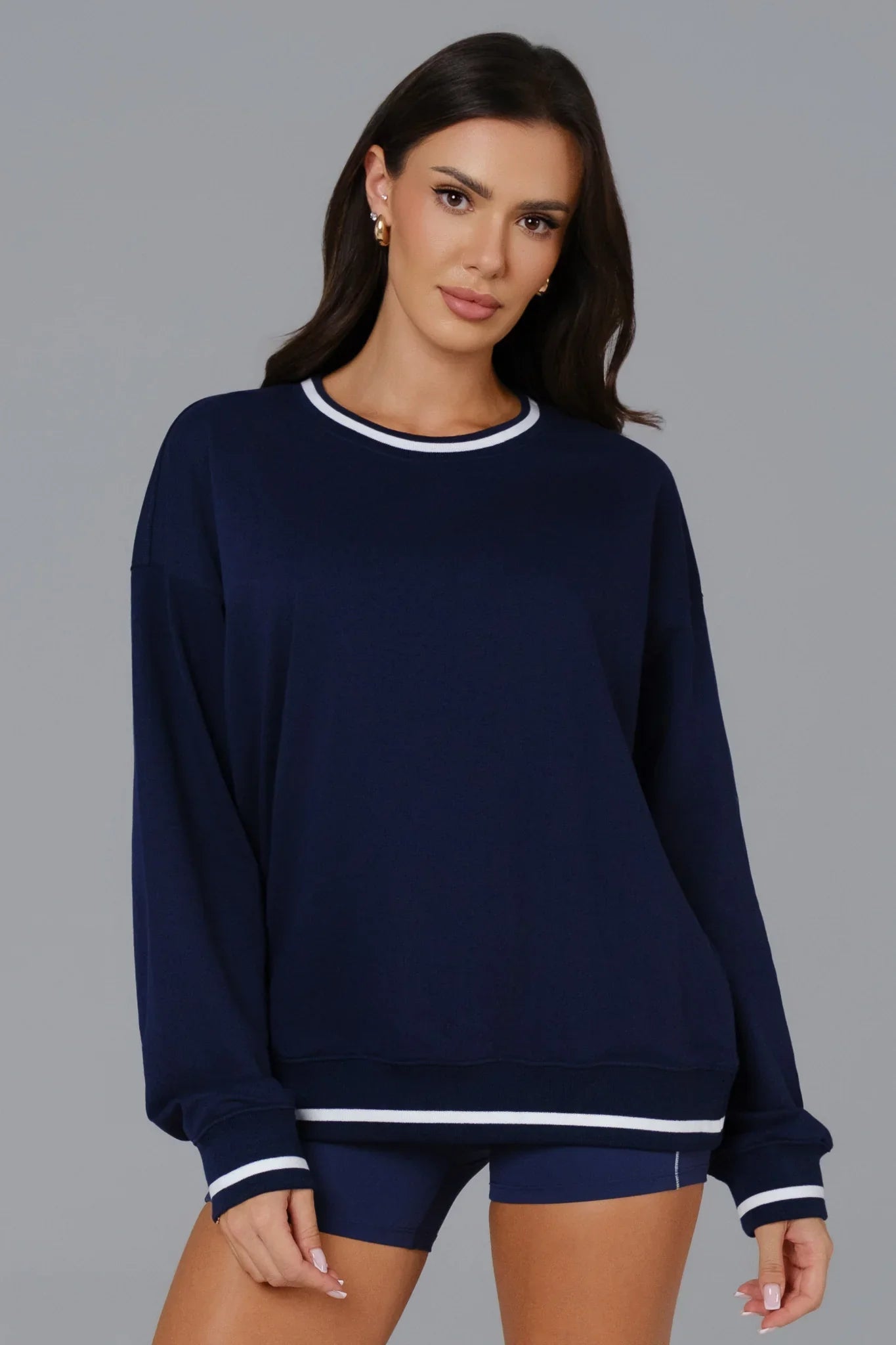 Woman wearing a navy blue sweater with white trim on a gray background