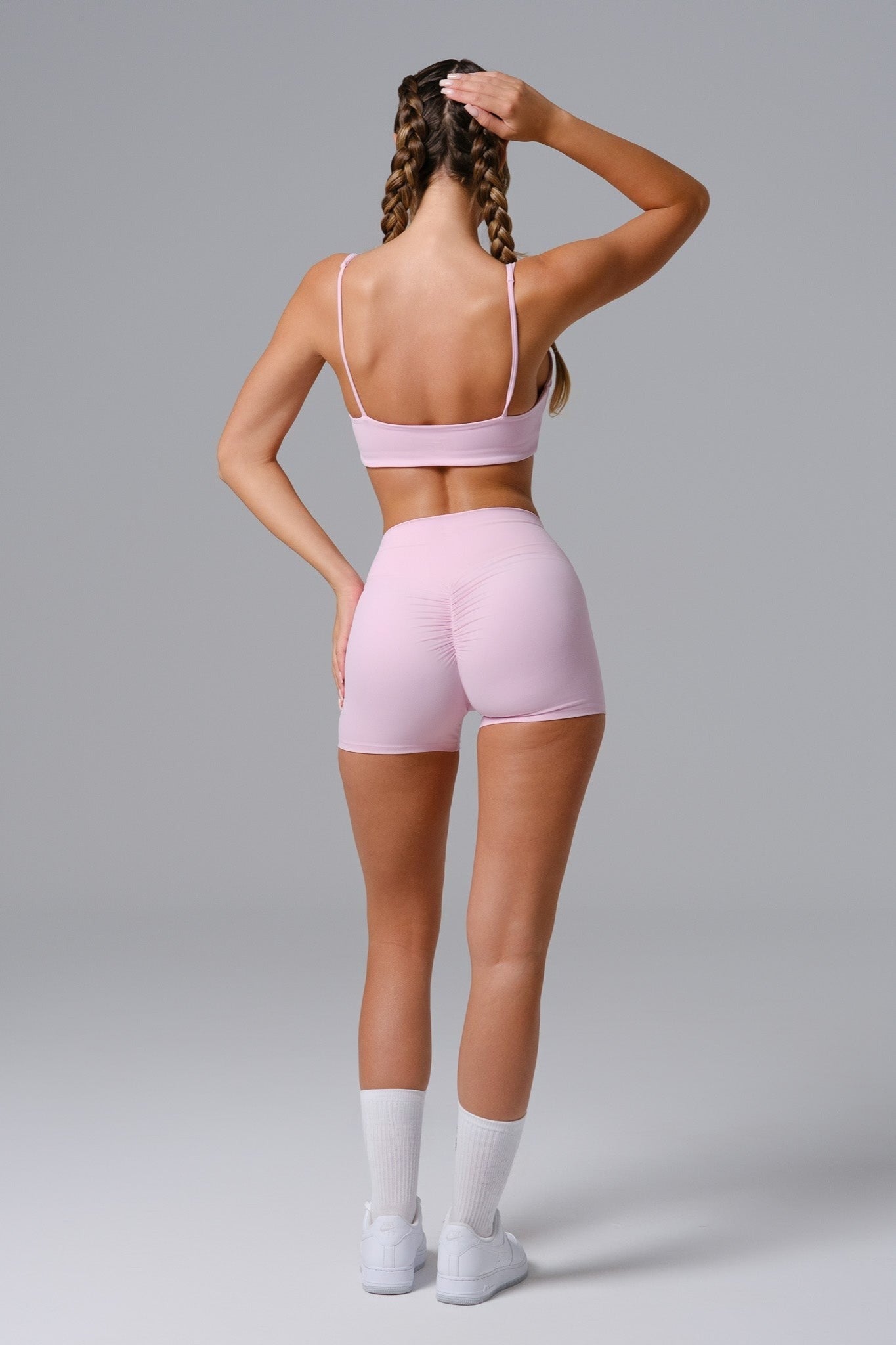 Person wearing a pink sports bra and shorts set on a gray background