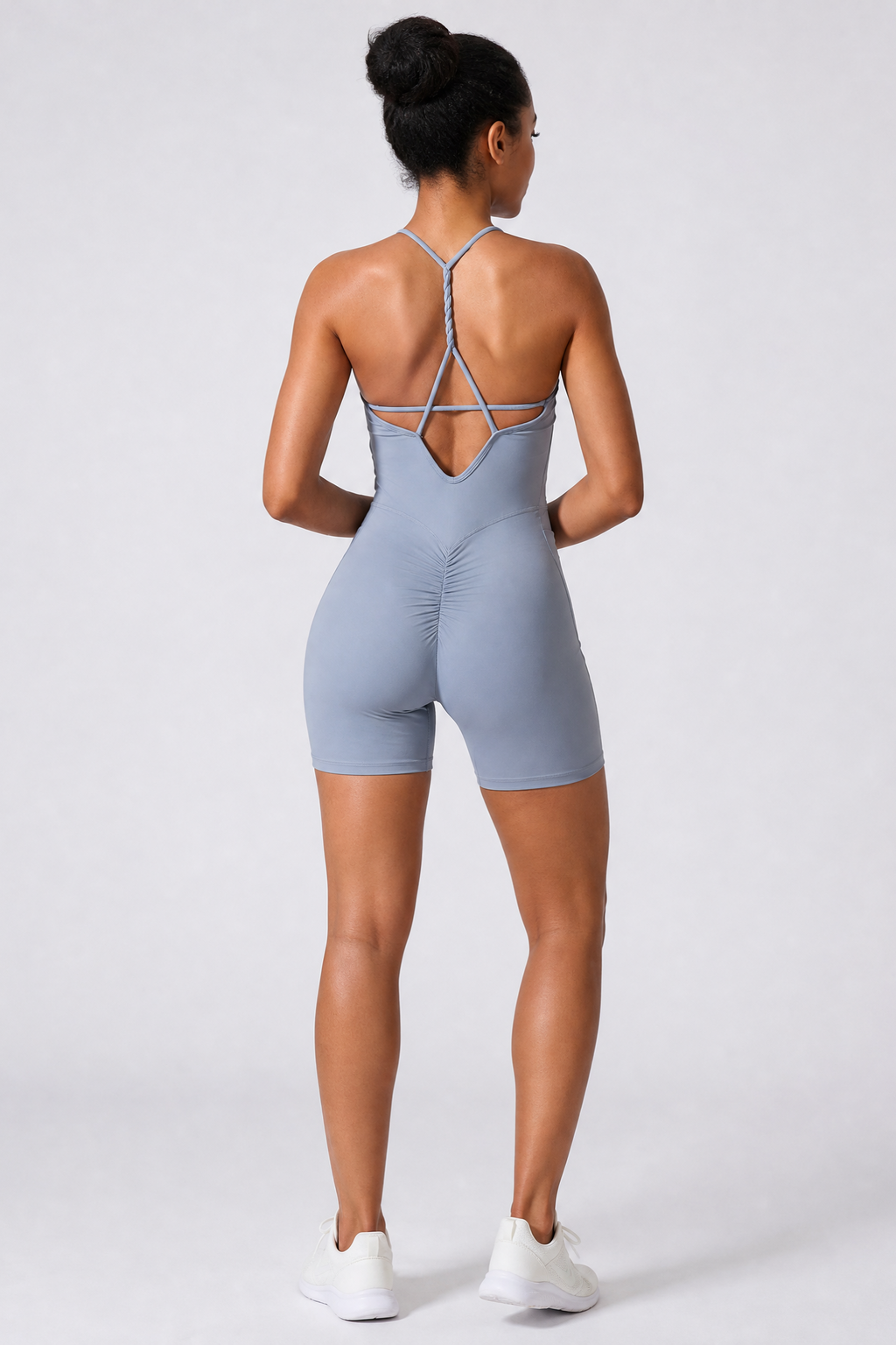 Person wearing a haze blue jumpsuit with criss-cross back design on a white background