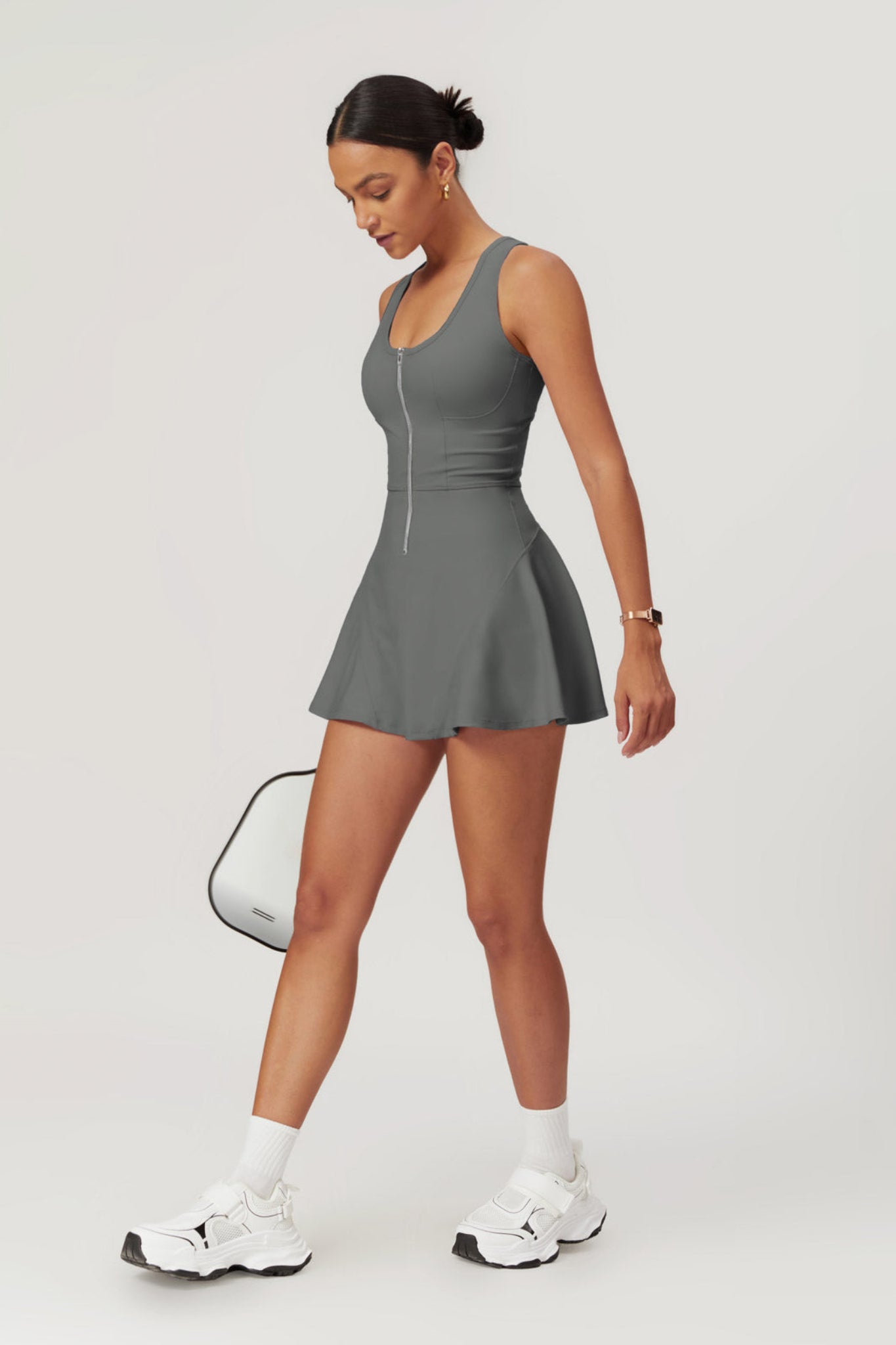 Woman wearing a gray dress with white sneakers on a light gray background